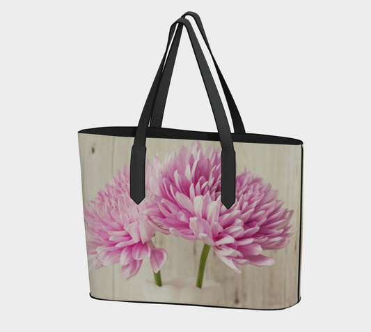 A vegan leather tote bag with a floral pattern featuring pink chrysanthemums, with solid black straps and base.