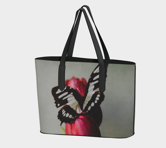 A vegan leather tote bag with a floral pattern featuring a butterfly on a tulip, with solid color straps and base in brown or black.