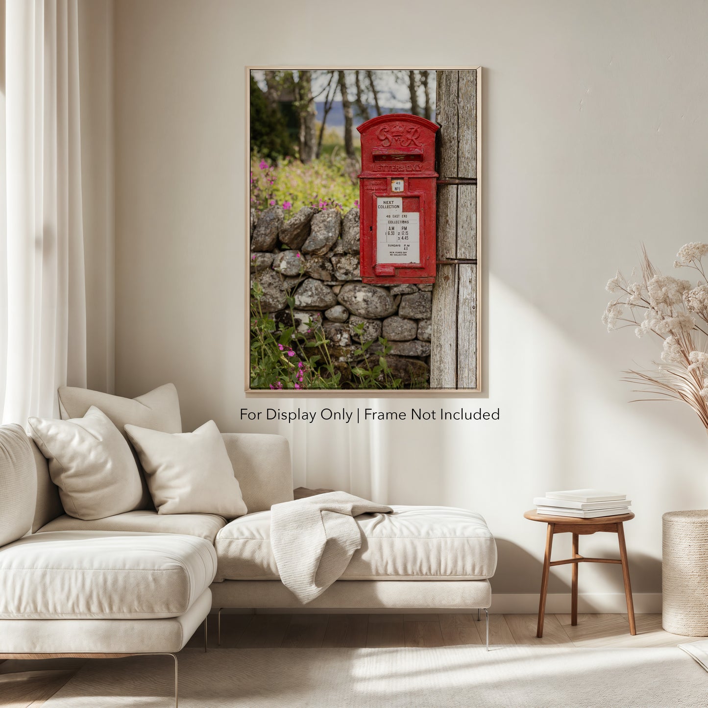 A classic red British post box mounted on a wooden pole beside a stone wall with wildflowers, photographed in soft countryside light.