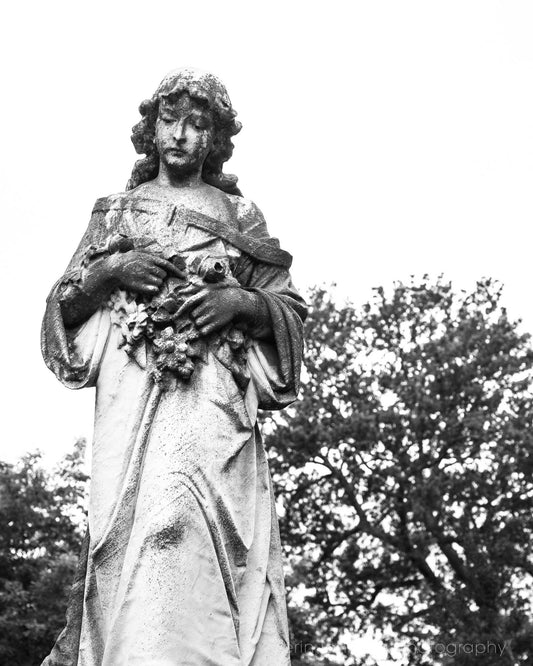 Black and white photograph of an angel statue holding a floral wreath, likely made from a print or canvas of the Oakland Cemetery in Atlanta, Georgia.