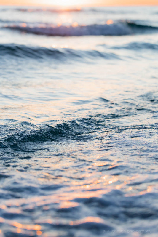 A close-up photograph of ocean waves with a soft focus, showing the gentle interplay of light and shadow.