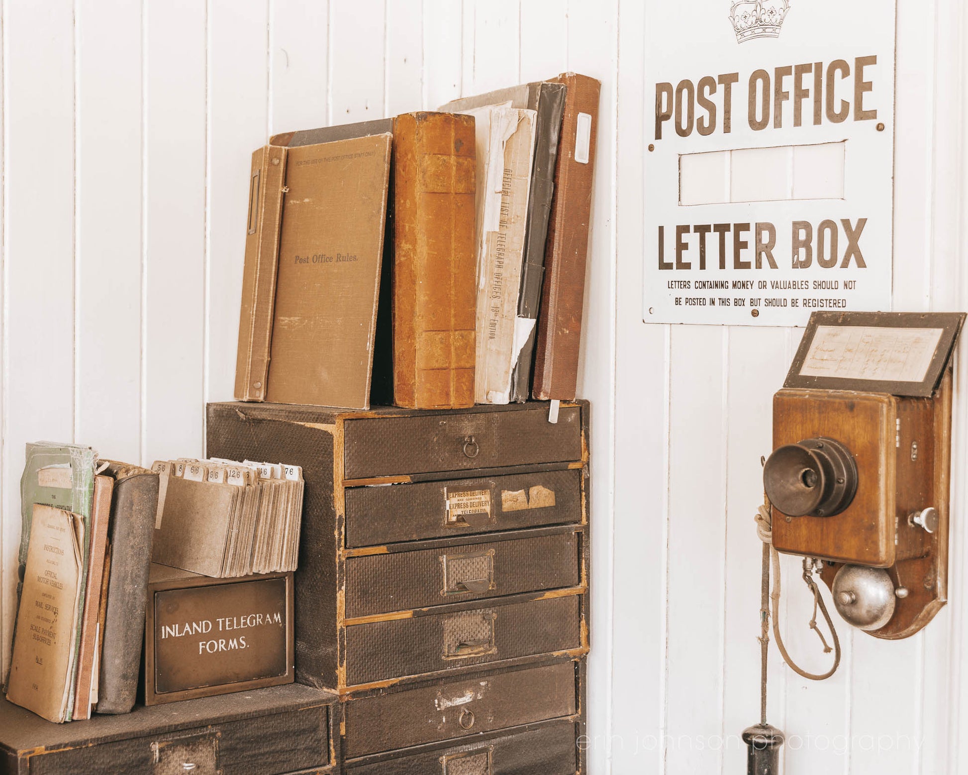 Vintage-style letter box and books on a wooden shelf against a white wall with a 'Post Office' sign.