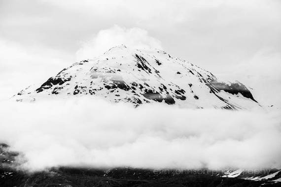 A black and white photograph of a mountain shrouded in fog with a cloudy sky above.