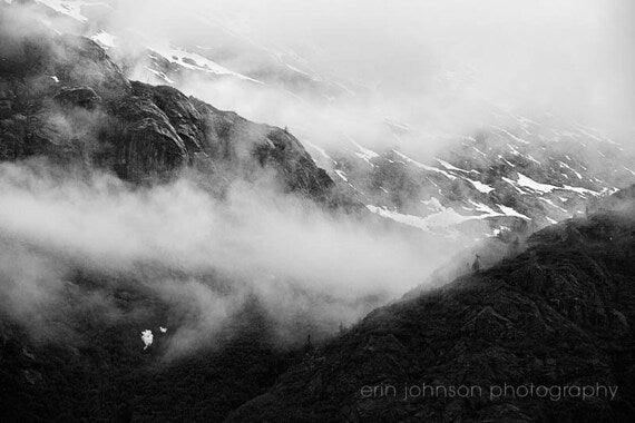 A black and white photograph featuring a misty landscape of snowy mountain peaks.