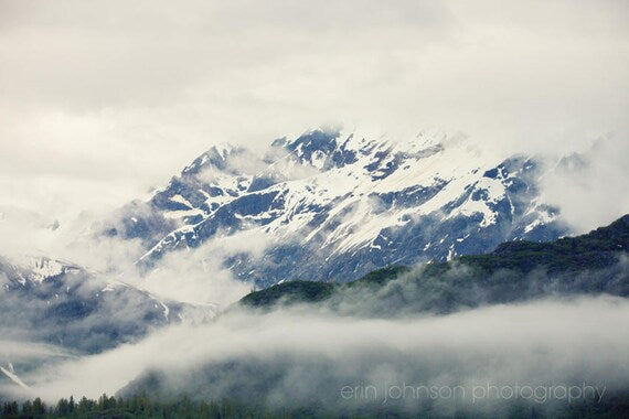 A photograph featuring snow-covered mountains with fog, indicative of a landscape in Alaska's Glacier Bay.