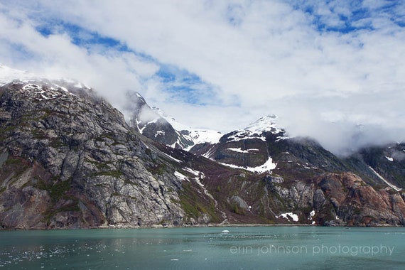 A landscape photograph featuring snow-covered mountains and a body of water in the foreground, with a blue sky overhead.