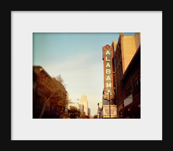 A photograph featuring the Alabama Theater in Birmingham, Alabama, with a vintage style movie sign on the side of a building.
