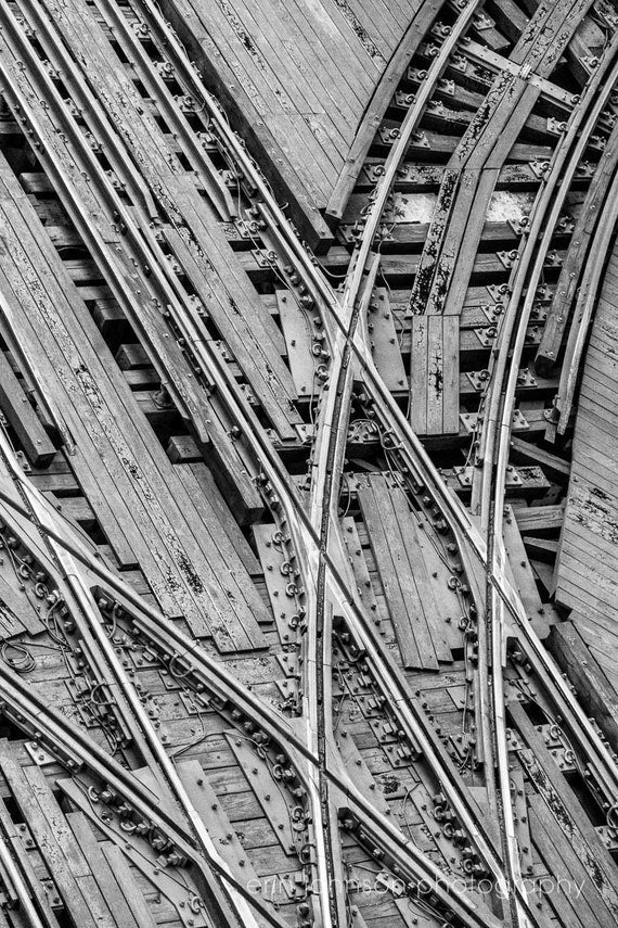 A high-resolution black and white photograph of Chicago's el train tracks, showcasing the intricate pattern and industrial aesthetic of the tracks against a wooden background.