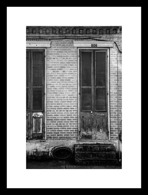A black and white photograph of a weathered door in the French Quarter, New Orleans, with the address '808' visible.