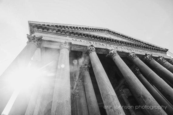 Black and white photograph of the Pantheon in Rome, highlighting the building's columns and dome with a sun flare in the background.