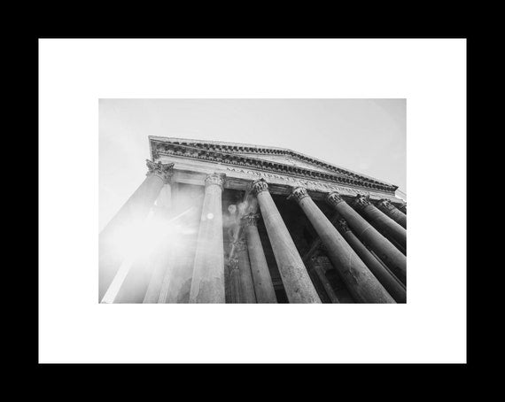 Black and white photograph of the Pantheon in Rome, highlighting the building's columns and dome with a sun flare in the background.