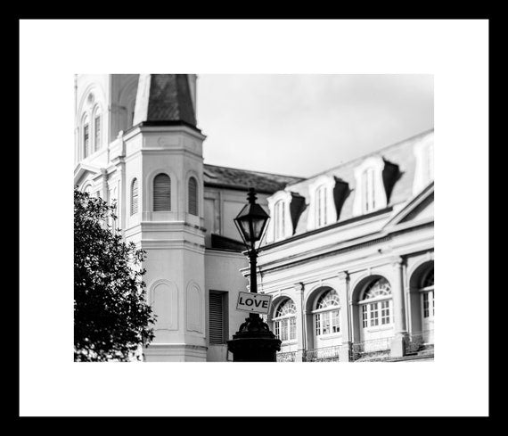 A black and white photograph of the St. Louis Cathedral in Jackson Square, New Orleans, with a 'LOVE' sign visible.