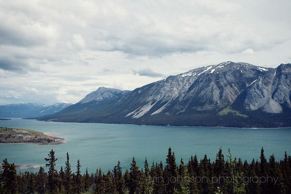A landscape photograph featuring a body of water with mountains in the background, under a grey sky.