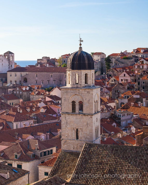 A photograph featuring a bell tower in the center with a clear view of the surrounding cityscape, showcasing the architecture and rooftops of Dubrovnik, Croatia.