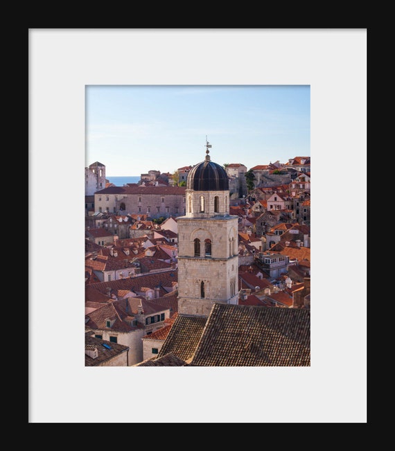 A photograph featuring a bell tower in the center with a clear view of the surrounding cityscape, showcasing the architecture and rooftops of Dubrovnik, Croatia.