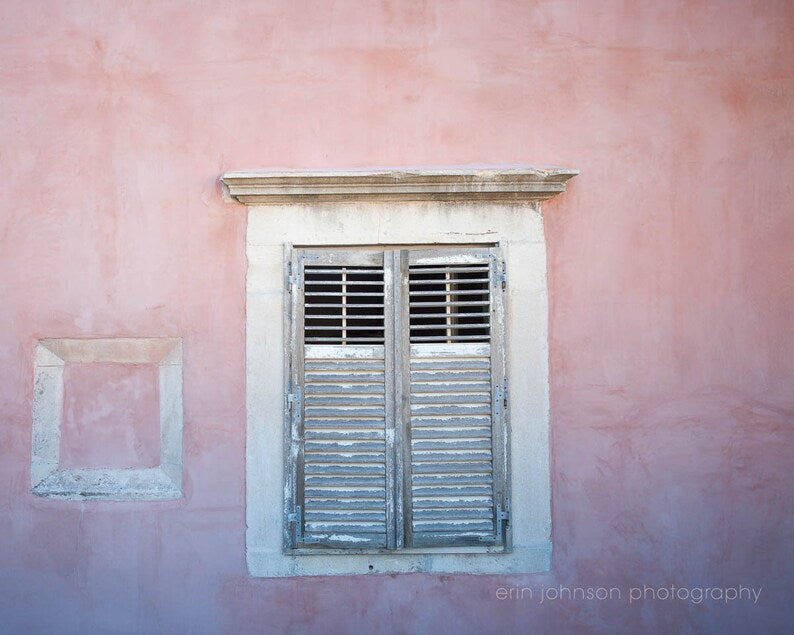 A photograph of a pink wall with a window and shutters in Dubrovnik, Crotia.