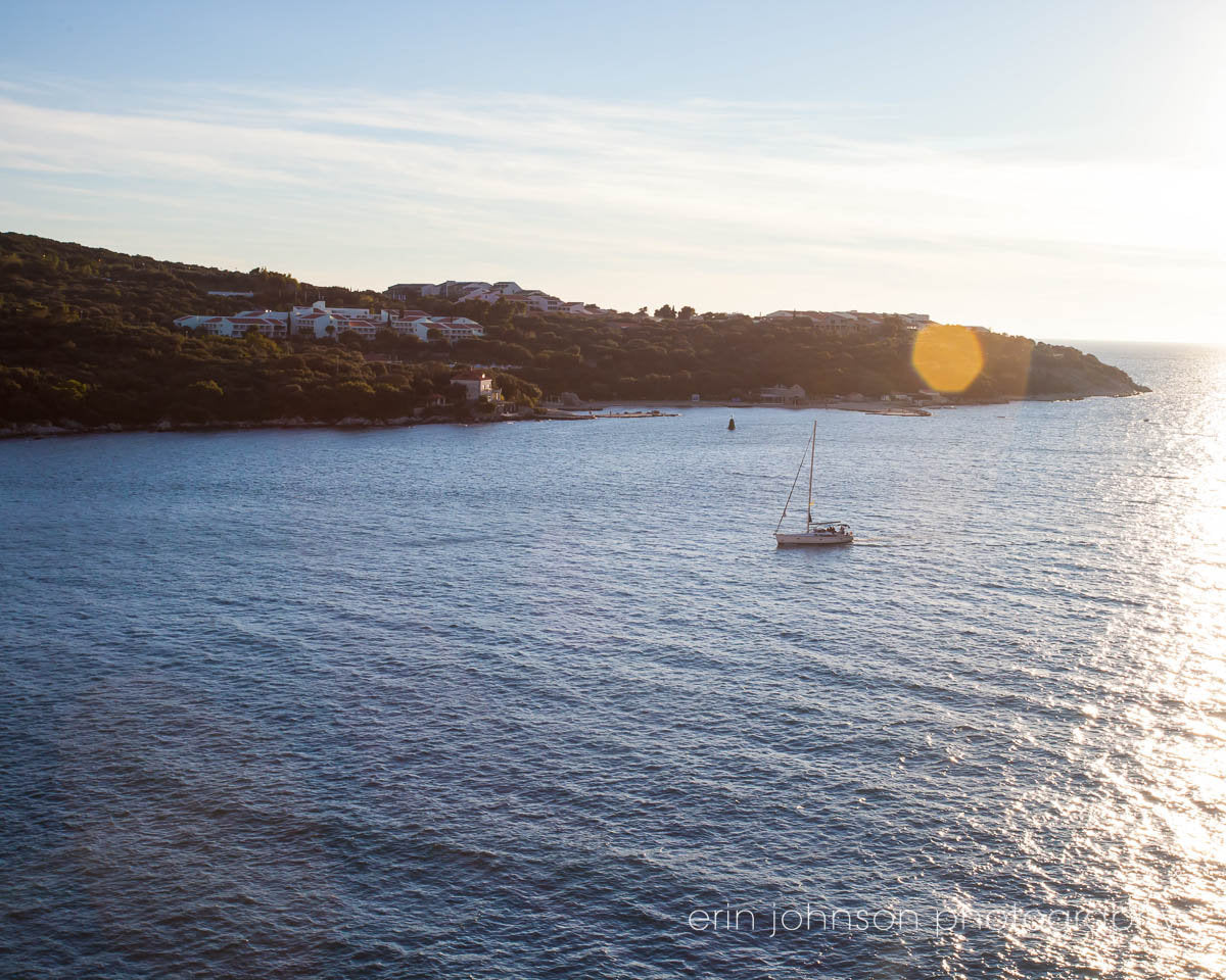 A landscape photograph featuring a sailboat on the water with a vibrant sunset in the background