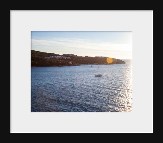 A photograph featuring a sailboat on the water with a vibrant sunset in the background