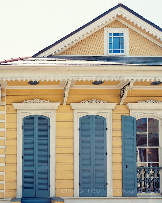 A photograph featuring a yellow and blue colored house with shutters, reflecting a typical New Orleans architectural style, with a watermark indicating the photographer is Erin Johnson.