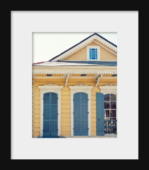 A photograph featuring a yellow and blue colored house with shutters, reflecting a typical New Orleans architectural style, with a watermark indicating the photographer is Erin Johnson.