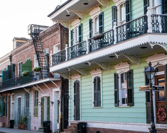 A photograph featuring a colorful row of buildings on a street corner in the French Quarter of New Orleans, with a decorative lamp post and a fire escape ladder.