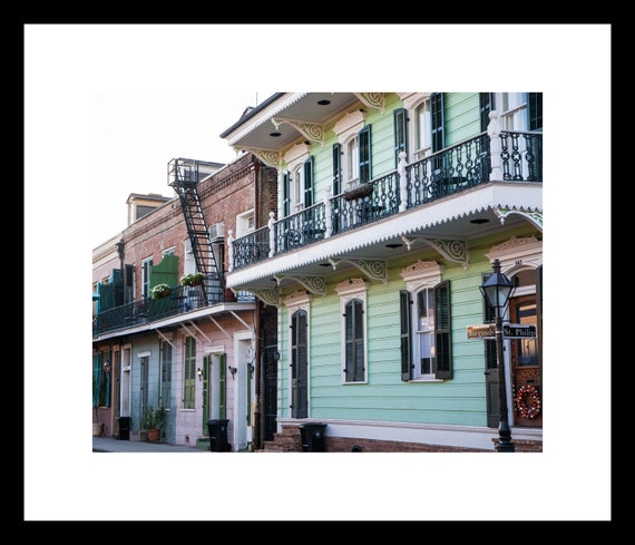 A photograph featuring a colorful row of buildings on a street corner in the French Quarter of New Orleans, with a decorative lamp post and a fire escape ladder.