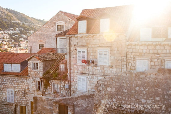 A photograph featuring sunlit rooftops in Dubrovnik, Croatia with a clear blue sky in the background.
