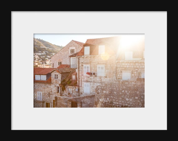 A photograph featuring sunlit rooftops in Dubrovnik, Croatia with a clear blue sky in the background.