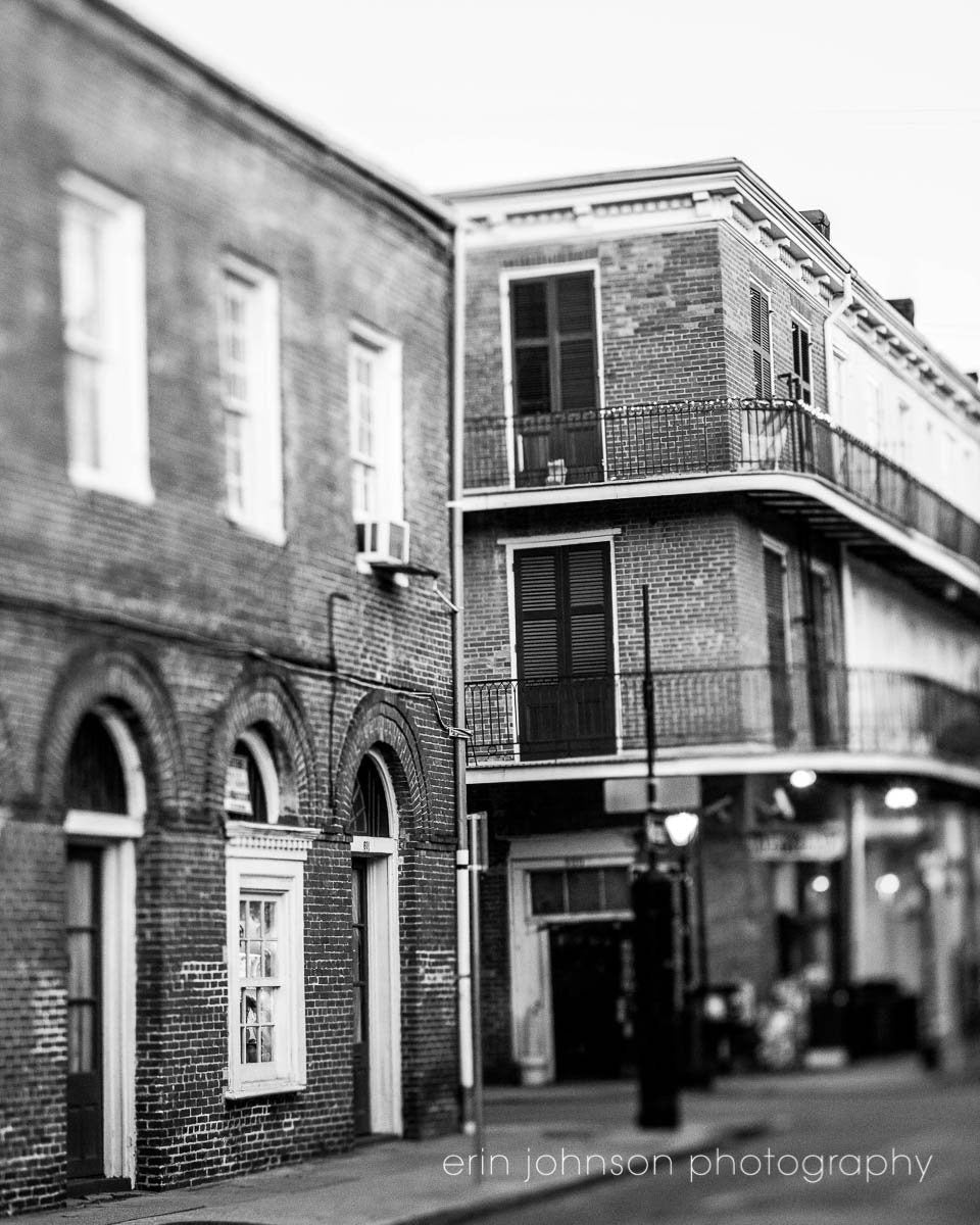 A black and white photo featuring a narrow street in the French Quarter, with architectural details