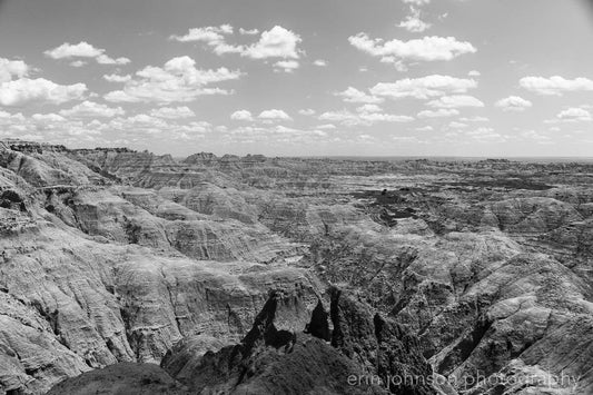 A black and white photograph of the Pinnacles Overlook in the Badlands National Park, with cloudy skies and rugged terrain.