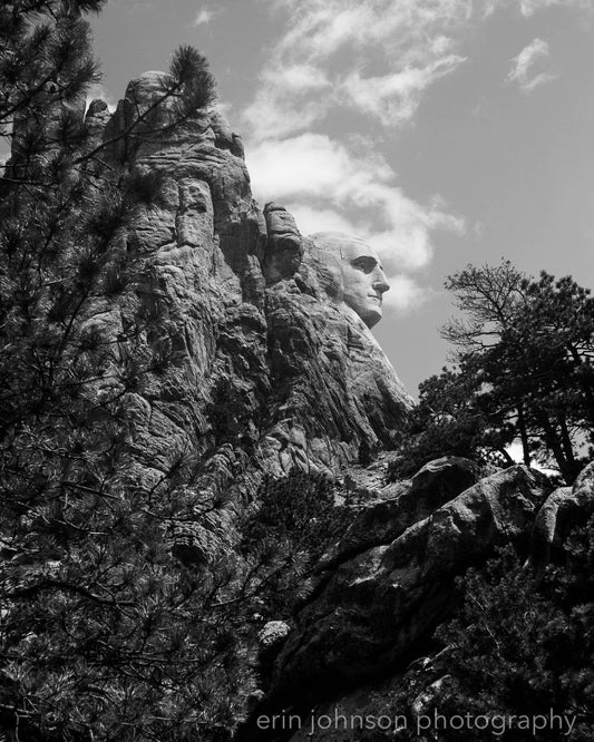 Black and white photograph of Mount Rushmore with George Washington's profile, trees in the foreground.