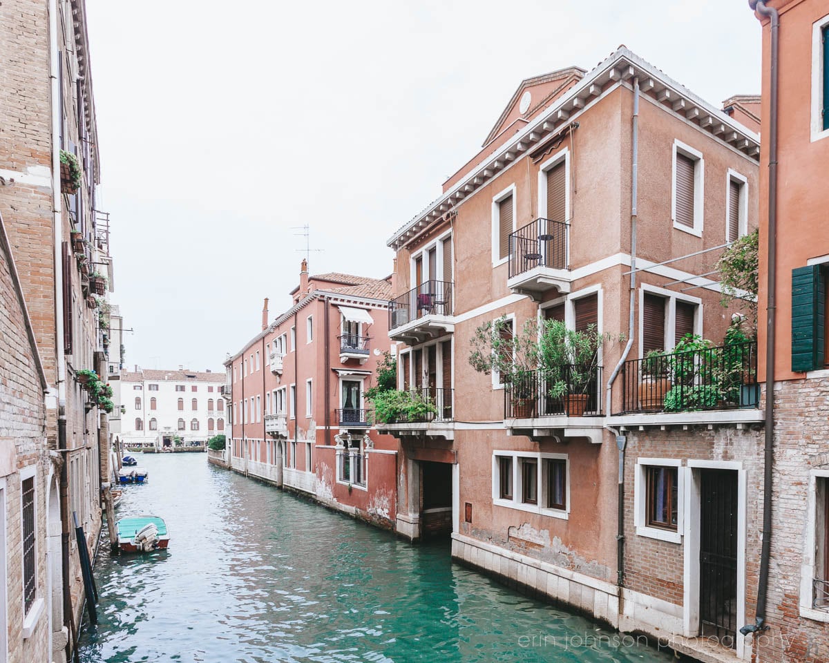A photograph featuring a narrow, winding waterway in Venice, Italy, with tall, colorful buildings on either side.