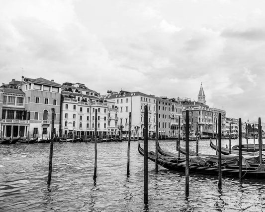 A black and white photograph of Venice, Italy, featuring the city's architecture along a waterway with boats and gondolas.