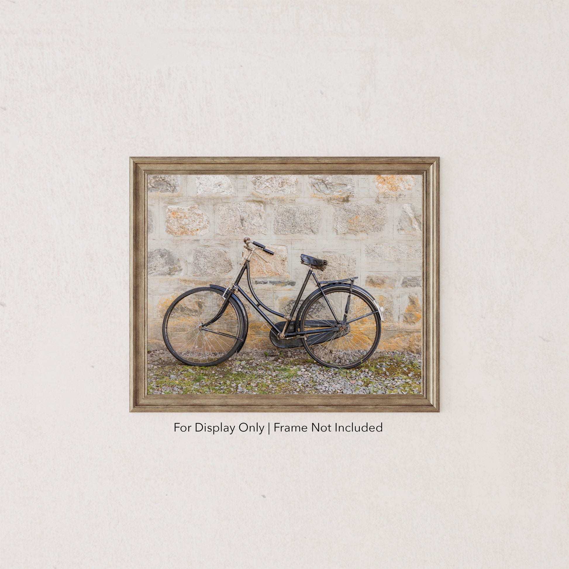 Vintage black bicycle leaning against a weathered stone wall, rustic countryside photography in neutral tones.