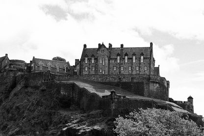 Black-and-white photograph of Edinburgh Castle perched on Castle Rock in Scotland, with dramatic stone walls and historic architecture.