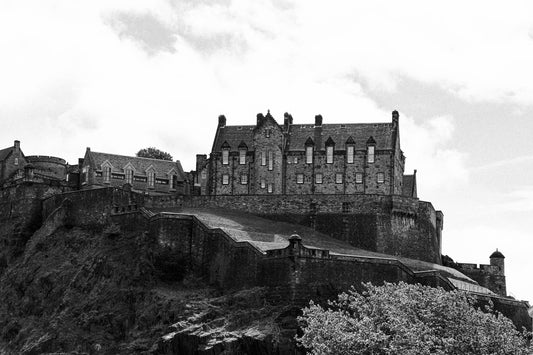 Black-and-white photograph of Edinburgh Castle perched on Castle Rock in Scotland, with dramatic stone walls and historic architecture.