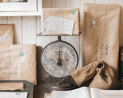 Rustic still life of vintage parcels wrapped in brown paper with stamps, stacked around a weathered post office scale.