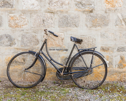 Vintage black bicycle leaning against a weathered stone wall, rustic countryside photography in neutral tones.