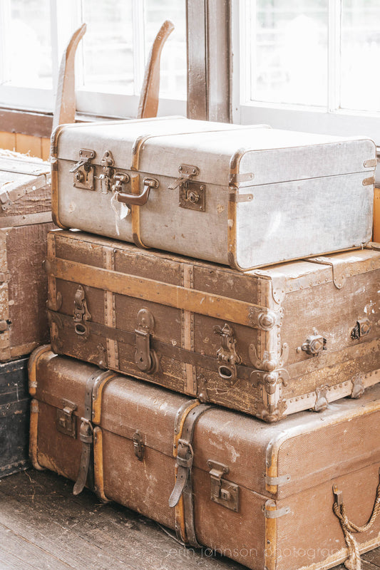 Stack of vintage suitcases and trunks with worn leather and metal details, photographed in soft natural light for a warm, rustic aesthetic.