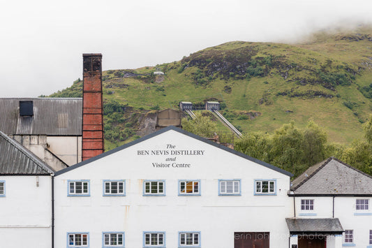 Ben Nevis Distillery and Visitor Centre in Fort William, Scotland, with whitewashed walls, red brick chimney, and Highland hills in the background.