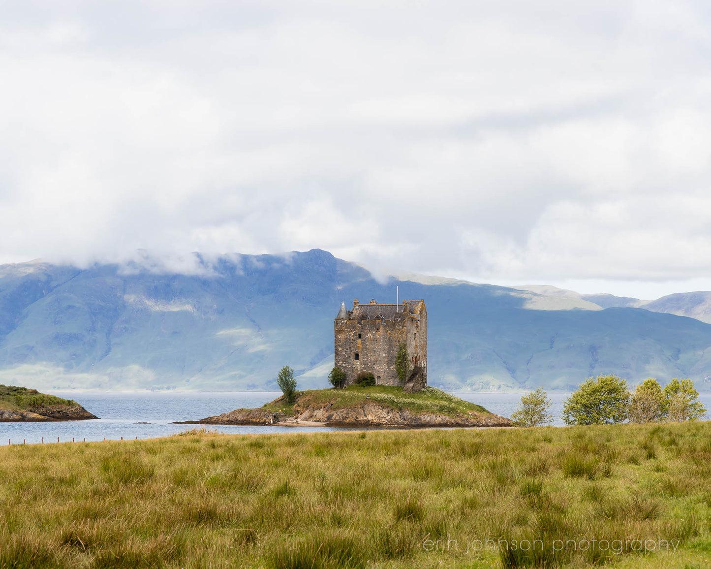 Castle Stalker on a small island in Loch Laich, Scottish Highlands, surrounded by mountains and water.