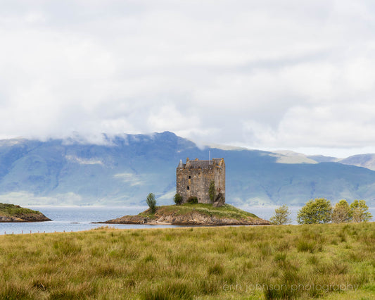 Castle Stalker on a small island in Loch Laich, Scottish Highlands, surrounded by mountains and water.