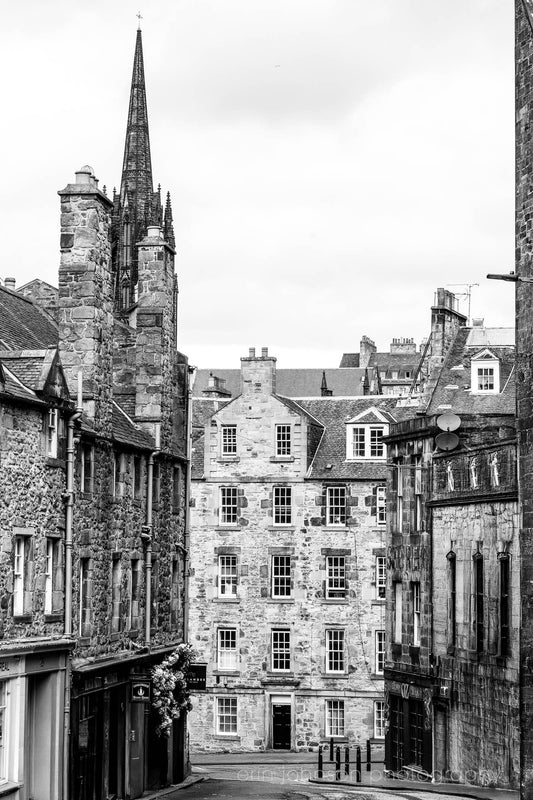 Black and white photograph of an Edinburgh street with historic stone architecture and a church spire.