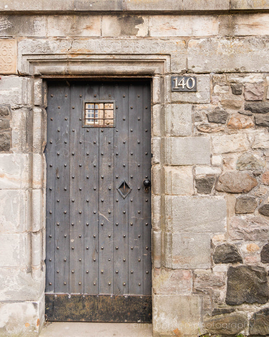 Rustic wooden door with iron studs set in a weathered stone wall, photographed in Edinburgh, Scotland.