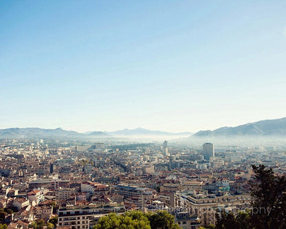 A photograph depicting the skyline of Marseille, France, with a clear blue sky and distant mountains.