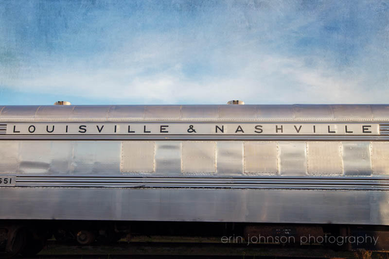 a silver train traveling down train tracks under a blue sky