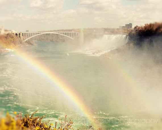 a rainbow in the middle of a waterfall with a bridge in the background