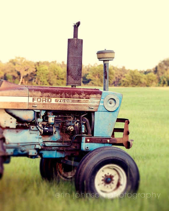 an old blue tractor sitting in the middle of a field
