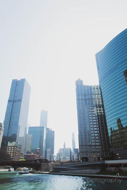 A photograph featuring a skyline of skyscrapers along the Chicago river, reflecting a cityscape, with a clear blue sky overhead.